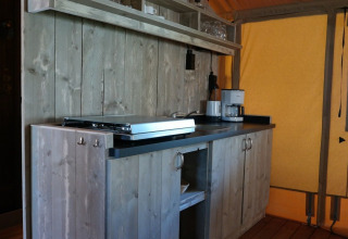Zona de cocina dentro de una tienda safari de lujo con muebles de madera y cafetera en De Kleine Belties.
