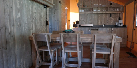 Vista interior de la tienda safari Luxury Lodge con mesa de madera y cocina en De Kleine Belties, Países Bajos.