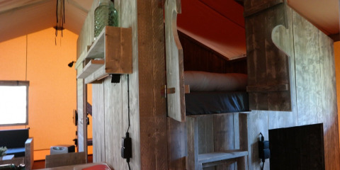 Binnenzicht van een luxe safaritent met houten stapelbed en kast in een vakantiepark in Nederland.