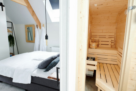 Bedroom with a double bed and wooden sauna at Wellness Lodge, Holiday Park De IJsvogel in the Netherlands.
