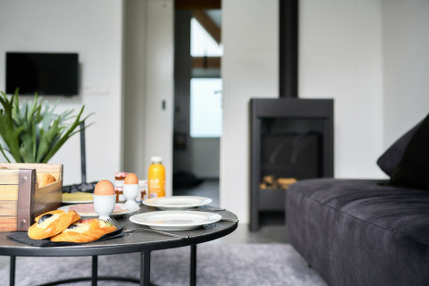 Wohnzimmer der Wellness Lodge im Holiday Park De IJsvogel mit Frühstück, schwarzem Sofa und Kamin.