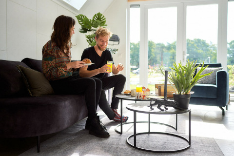 Two people enjoy breakfast inside the Wellness Lodge at Holiday Park De IJsvogel, Netherlands, sunlight streaming in.
