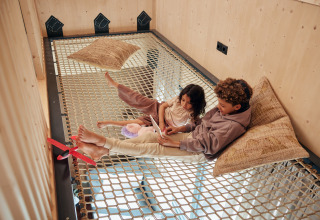 Twee kinderen ontspannen op een net met kussens en tablet in Unbrick One | Sauna te Brinckerduyn, Nederland.
