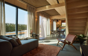 Interior de lodge moderno con grandes ventanales, paneles de madera, muebles cómodos y vistas exteriores.