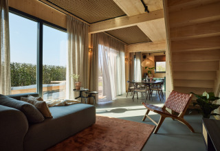 Hedendaags lodge-interieur met grote ramen, houten afwerking, gezellige meubels en tuinzicht in Nederland.