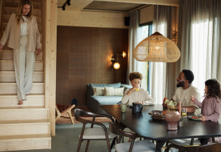 Een gezin ontbijt in een moderne lodge terwijl een vrouw de trap afdaalt bij Unbrick One, Brinckerduyn, Nederland.