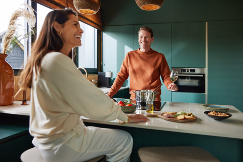 Dos personas sonrientes disfrutan un momento acogedor en la cocina en Unbrick One | Sauna en Brinckerduyn, Países Bajos.