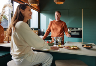 Twee lachende personen hebben een gezellig moment in de keuken bij Unbrick One | Sauna in Brinckerduyn, Nederland.