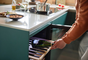 A person takes a wine bottle from a wine fridge in a modern kitchen at Unbrick One | Sauna at Brinckerduyn, Netherlands.