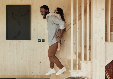 Hombre lleva a un niño en la espalda en un moderno lodge de madera en Unbrick One | Sauna en Brinckerduyn, Países Bajos.