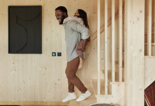 Man draagt een kind op zijn rug in een moderne houten lodge bij Unbrick One | Sauna in Brinckerduyn, Nederland.