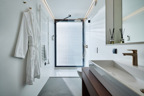 Baño moderno con ducha, bata blanca, detalles en madera y grifería dorada en Unbrick One, Países Bajos.
