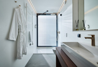 Modern bathroom with walk-in shower, white robe, wood accents, and gold faucet at Unbrick One in the Netherlands.