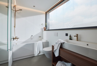 Modern, helder badkamer met groot raam, bad en houten elementen in Unbrick One | Sauna, Brinckerduyn.