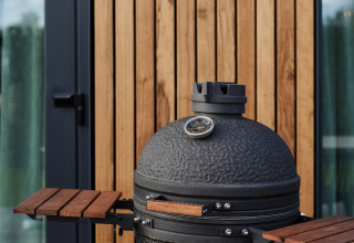 Zwarte keramische barbecue met thermometer voor houten panelen aan een moderne lodge met glazen deur.