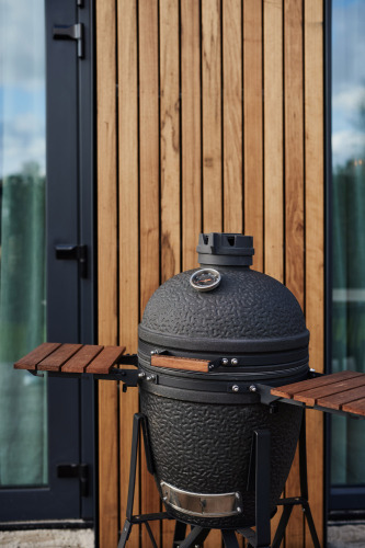 Zwarte keramische barbecue met thermometer voor houten panelen bij een moderne lodge met glazen deur.