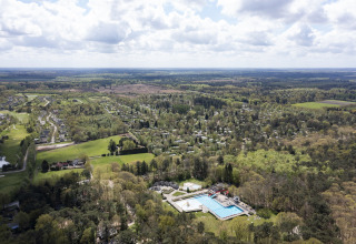 Luchtfoto van een lodge met zwembad, omringd door bossen en verspreide huisjes onder een bewolkte hemel.