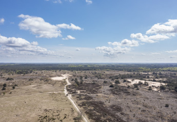 Vue aérienne d’un paysage de lande ouverte avec du sable, des sentiers et un ciel bleu près d’un lodge.