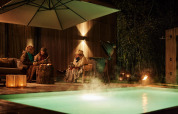 Tres personas conversan y disfrutan bebidas junto a una piscina iluminada en Unbrick One, Brinckerduyn, Países Bajos.