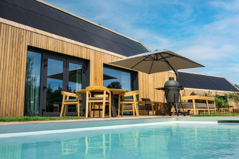Moderne lodge med trægavl, solpaneler, terrasse, pool og parasol på Brinckerduyn i Holland.