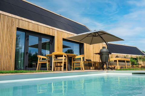 Moderne lodge i træ med solpaneler, udendørs møbler, parasol og pool ved Brinckerduyn i Holland.