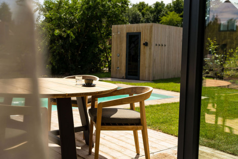 Terraza exterior con mesa y sillas de madera, vista a la piscina y sauna en Unbrick One en Brinckerduyn, Países Bajos.