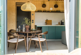 Espace repas moderne et cuisine à la lodge Unbrick One avec meubles en bois, placards verts et lumière douce.