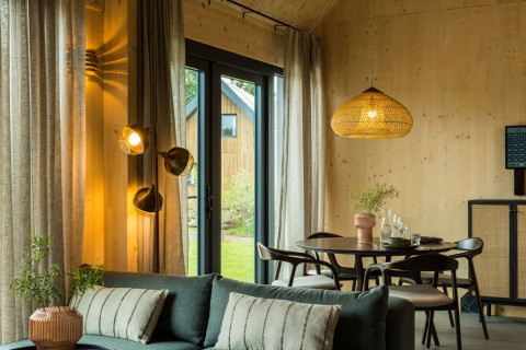 Modernes Lodge-Interieur mit Holzverkleidung, Essbereich, Sofa und großen Fenstern im Brinckerduyn, Niederlande.