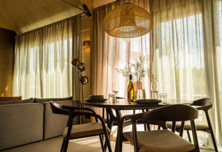 Comedor moderno con sillas de madera, luz natural y cortinas de lino en Unbrick One Lodge, Países Bajos.