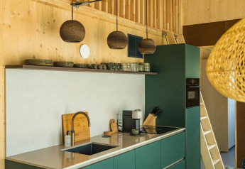Cocina moderna con gabinetes verdes, paneles de madera y lámparas colgantes en Unbrick One, Países Bajos.