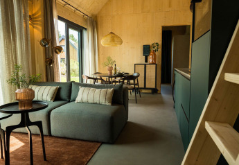 Salón de lodge moderno con sofá verde, mesa de comedor y grandes ventanales en Unbrick One | Sauna and Pool, Brinckerduyn.