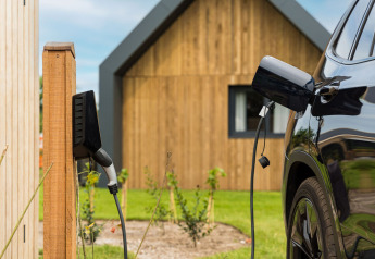 Elektrische wagen laadt op aan laadpaal bij houten lodge in Unbrick One | Sauna en Pool Brinckerduyn, Nederland.