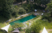 Aerial view of a natural swimming pool surrounded by trees at Eco domaine Le Camp holiday park in Occitanie, France.