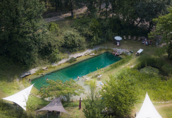 Luftfoto af naturlig swimmingpool omgivet af skov på Eco domaine Le Camp, feriepark i Occitanie, Frankrig.
