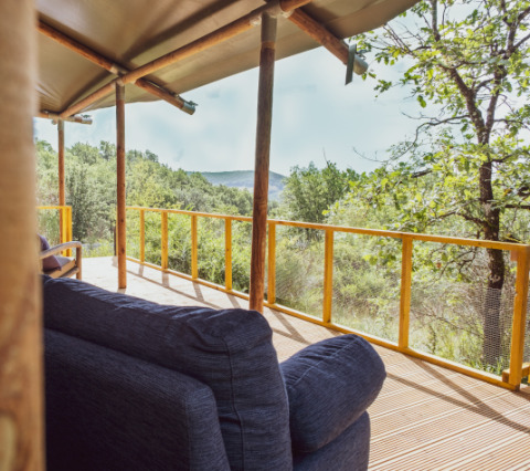 Cómoda terraza exterior de Lodgetent Samburu con vistas a colinas verdes y un bosque frondoso al fondo.
