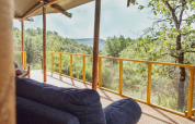 Gemütliche Veranda im Lodgetent Samburu mit Blick auf grüne Berge und bewaldete Landschaft in der Sonne.