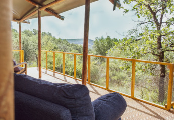 Cómoda terraza exterior de Lodgetent Samburu con vistas a colinas verdes y un bosque frondoso al fondo.