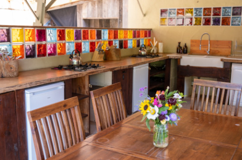 Kleurrijke keuken met houten tafel, bloemen en glasblokken in Eco domaine Le Camp, Occitanië, Frankrijk.