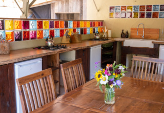 Farverig køkken med træbord, blomster og glasfliser i Eco domaine Le Camp i Occitanie, Frankrig.