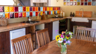 Cocina colorida con madera, azulejos de vidrio y flores en Eco domaine Le Camp, Occitanie, Francia.