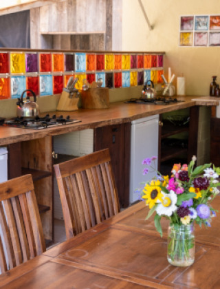 Cocina colorida con madera, azulejos de vidrio y flores en Eco domaine Le Camp, Occitanie, Francia.