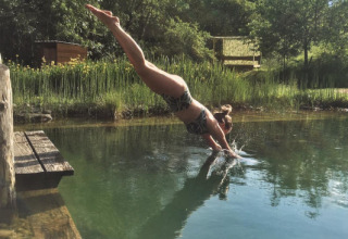 Kvinde dykker i naturlig swimmingpool omgivet af frodig natur i Eco domaine Le Camp, Occitanie, Frankrig.