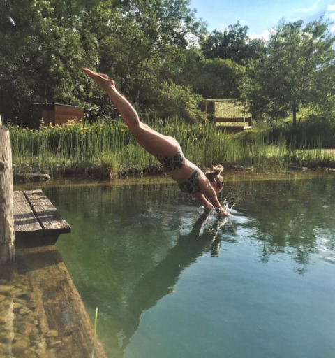 Frau springt in einen Naturpool im Eco domaine Le Camp, einem Ferienpark in Okzitanien, Frankreich.