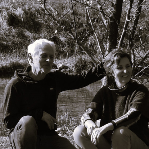 Two people sitting outdoors by a stream at Eco domaine Le Camp holiday park in Occitanie, France.