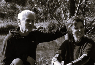 Zwei Menschen sitzen entspannt an einem Bach im Freien im Eco domaine Le Camp in Occitanie, Frankreich.