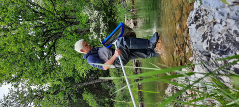 Person in Watstiefeln fischt am Ufer eines Sees, umgeben von Natur im Eco domaine Le Camp, Occitanie, Frankreich.