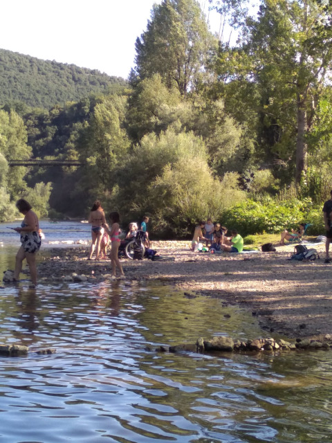 Menschen entspannen am Flussufer im Eco domaine Le Camp, einem Ferienpark in Occitanie, Frankreich.