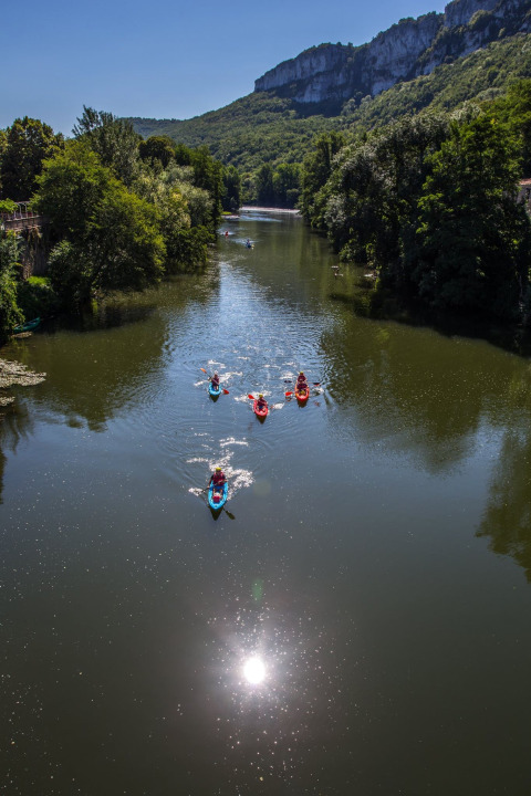 Kayakers paddling on a river near Varen, Occitanie, France, surrounded by trees and scenic cliffs.