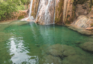 Beautiful waterfall surrounded by lush greenery near Varen, Occitanie, France, with clear turquoise water.