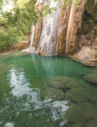 Hermosa cascada rodeada de vegetación cerca de Varen, Occitania, Francia, con agua cristalina y tranquila.